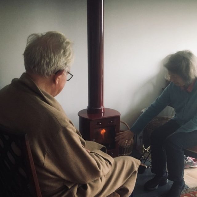 Two pensioners sitting by a fire, trying to warm up