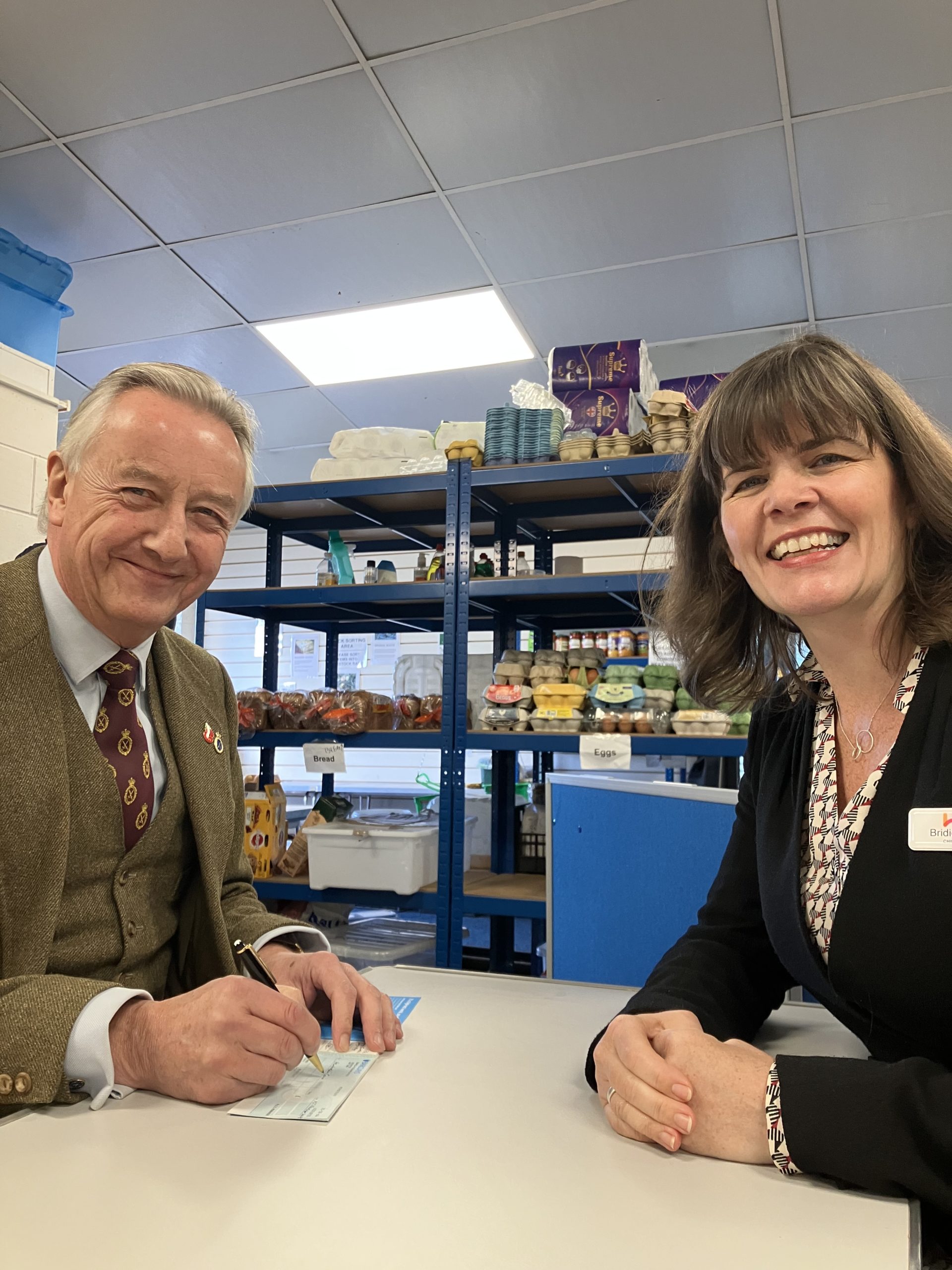 Robert Robinson at Ledbury Food Bank writing a cheque for the Surviving Winter appeal, accompanied by Bridie Sullivan from Herefordshire Community Foundation