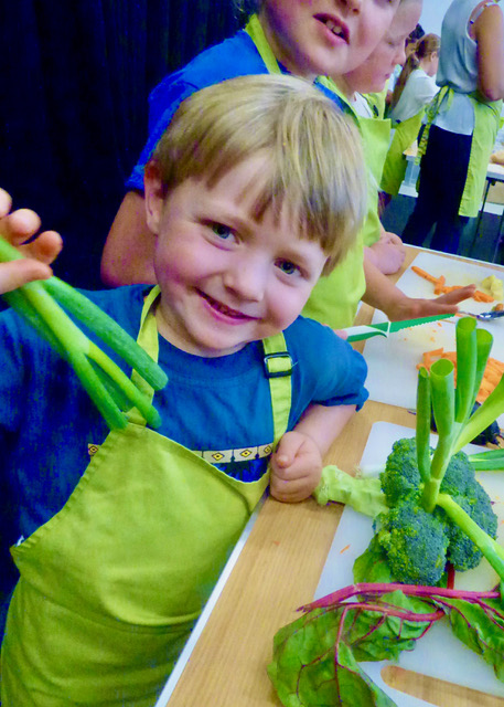 Little boy in a cooking workshop, holding up spring onions
